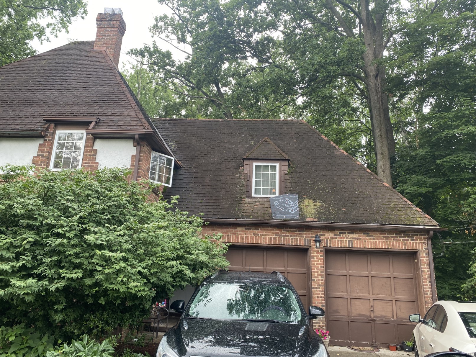A brick home with a garage and mature trees, car in the driveway