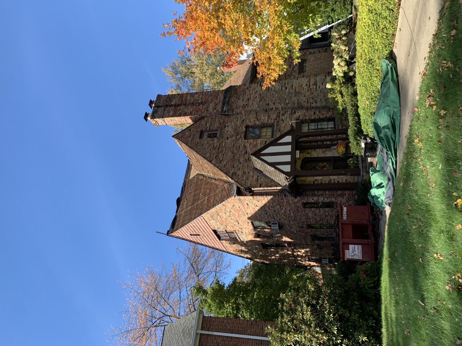 A brick Tudor home with a chimney and an autumn tree, exterior work by Santos Lopez Construction