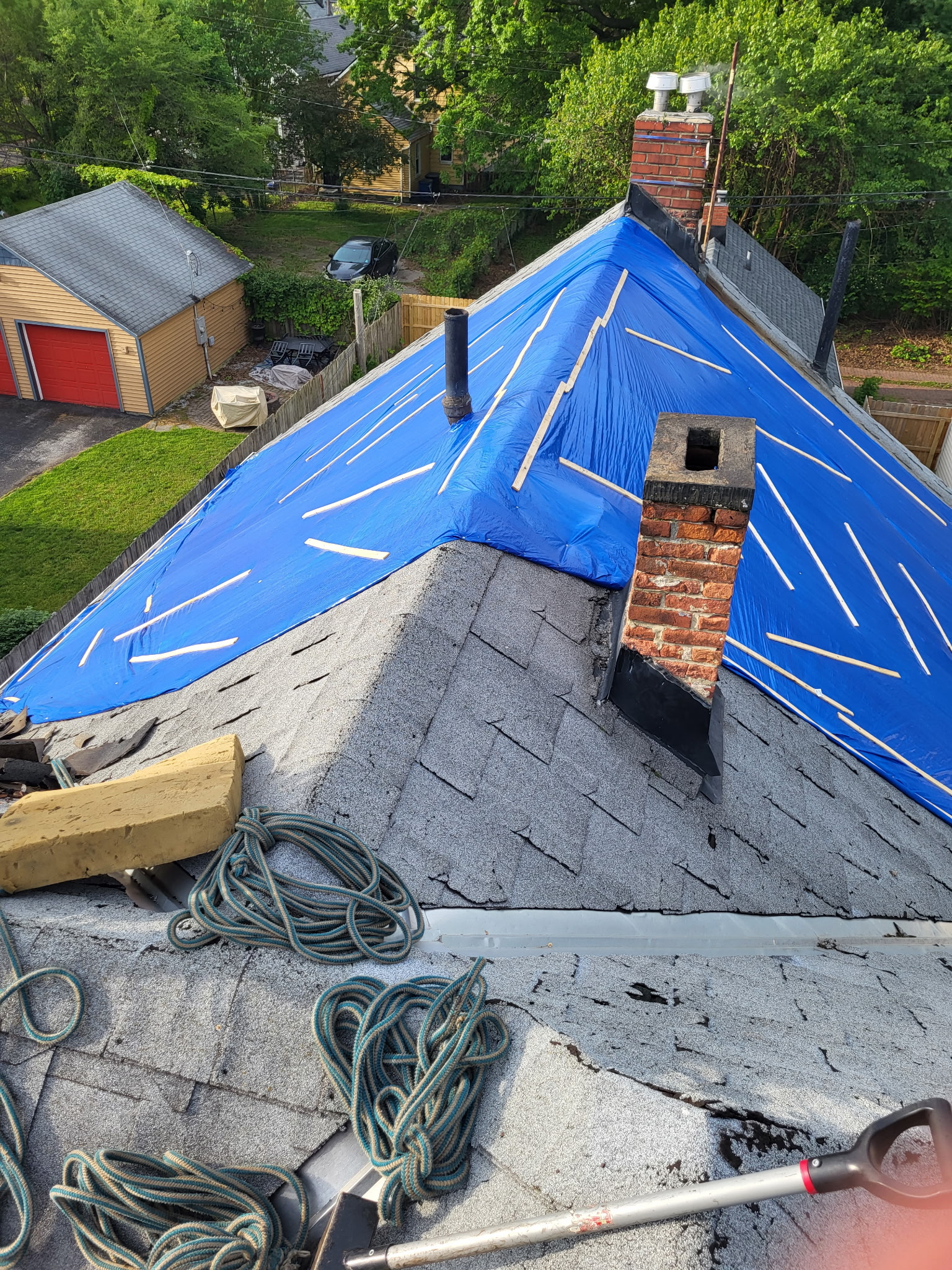 A storm-damaged roof protected under a blue emergency tarp before restoration by Santos Lopez Construction