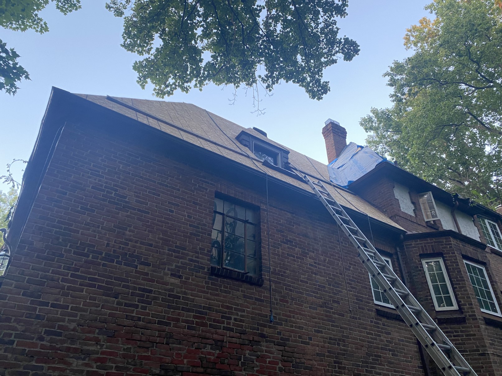 A steep roof mid-replacement with a ladder and neighboring homes behind