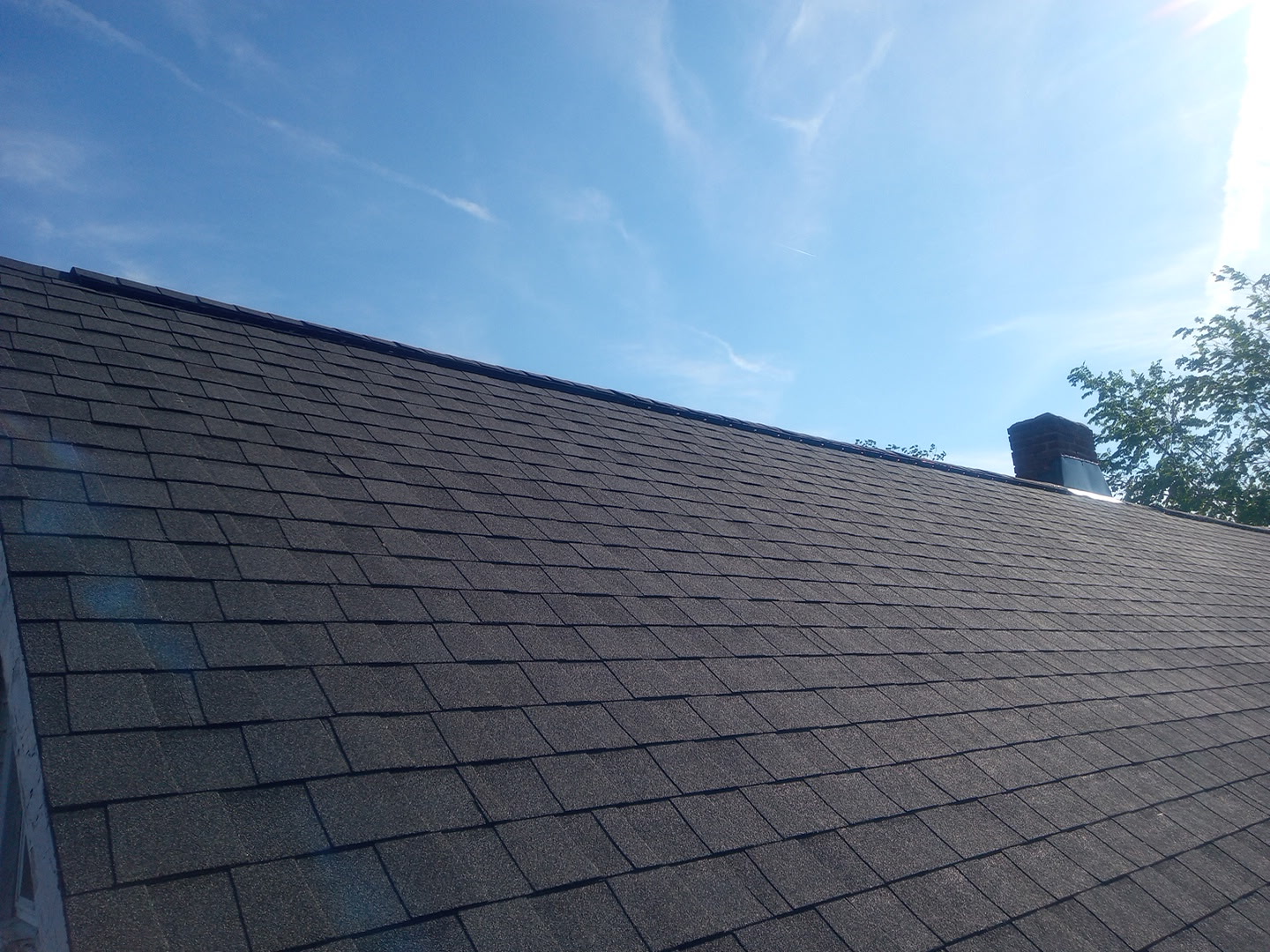 A dark new shingle roof plane against a clear blue sky
