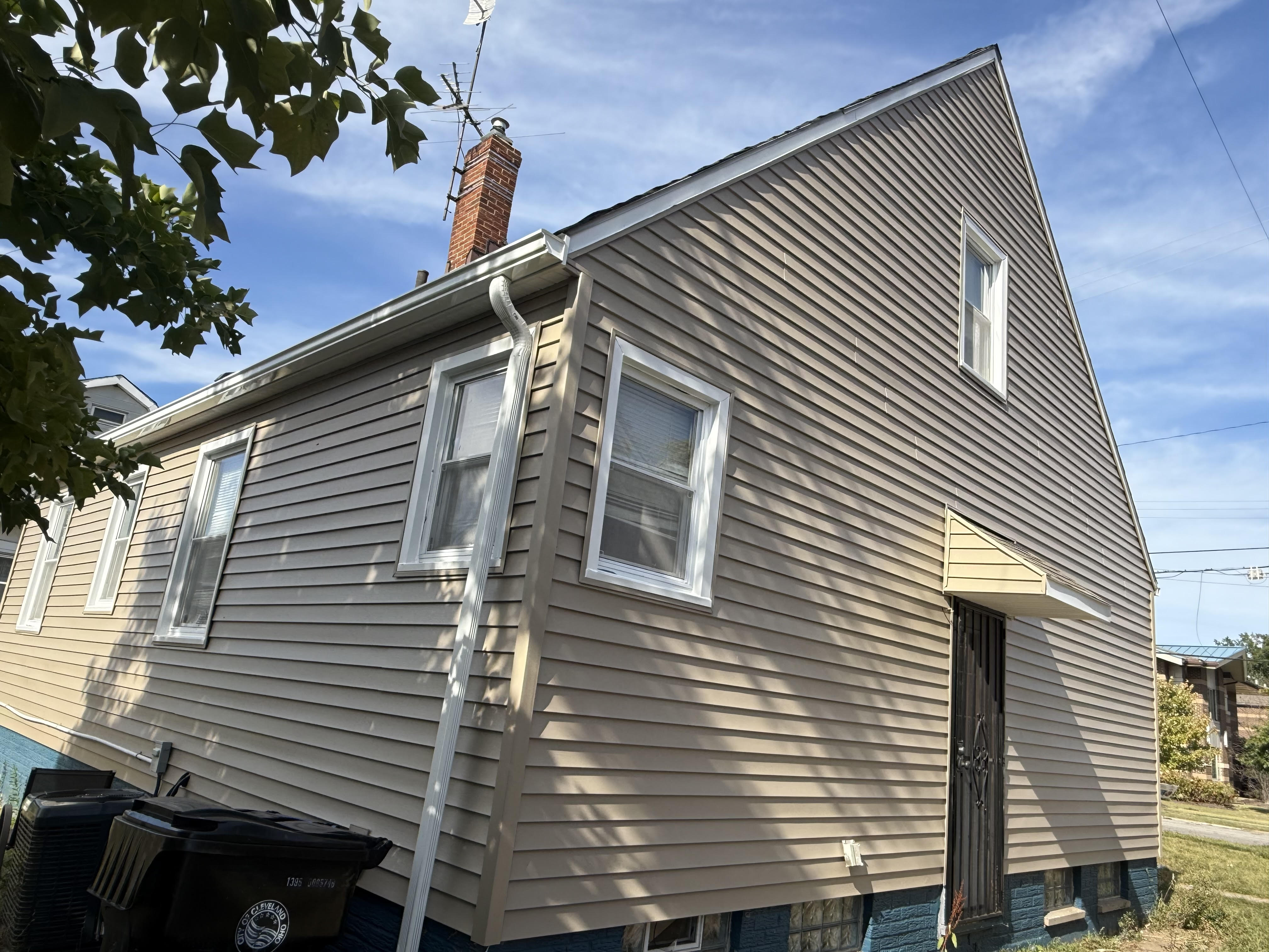 The side of a home with new tan and grey siding and a fresh downspout